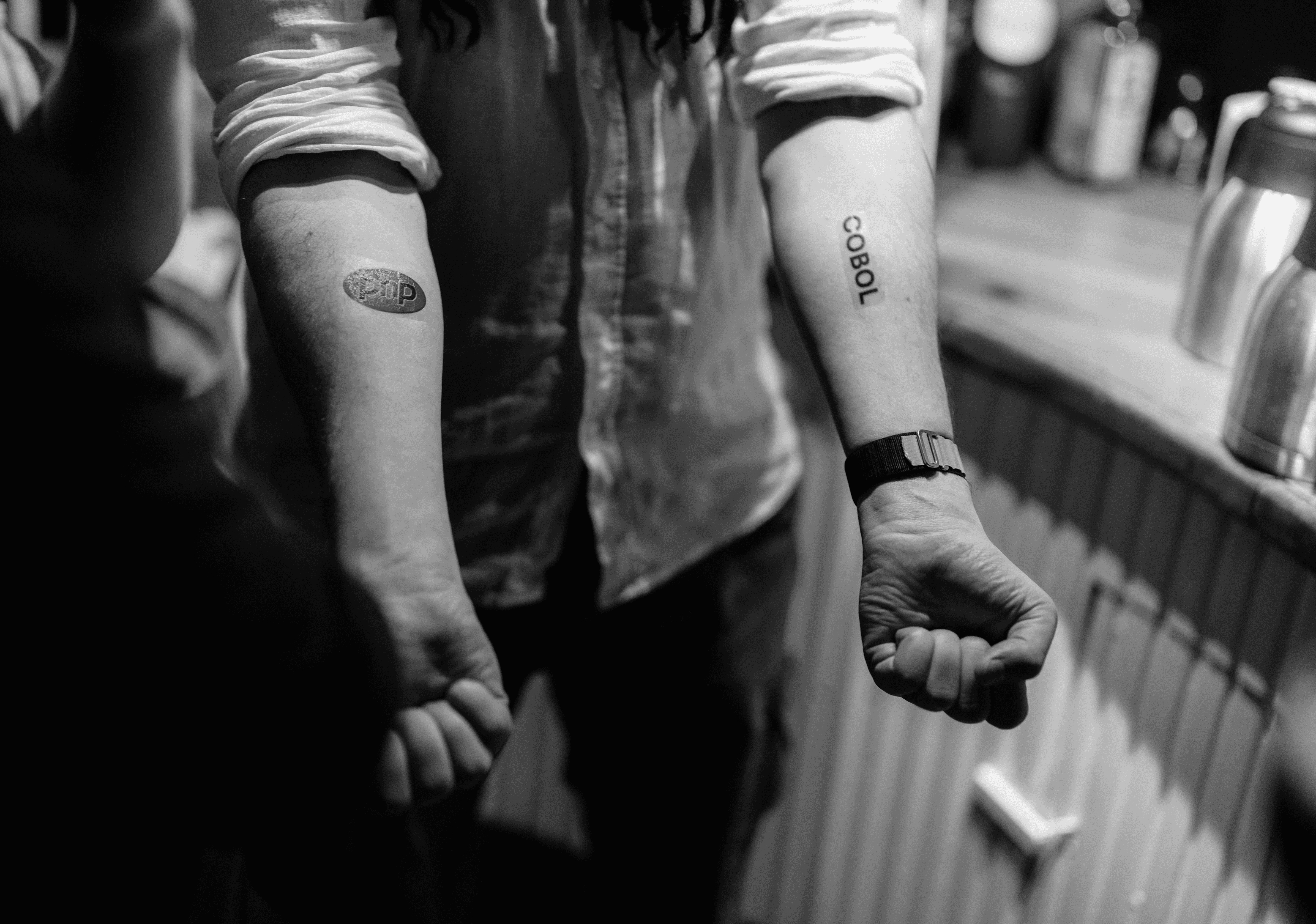 Person showing ‘PHP’ and ‘COBOL’ forearm tattoos, symbolizing tech skill and collaboration.